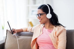 happy young woman sitting on sofa with tablet pc computer and headphones listening to podcasts at home