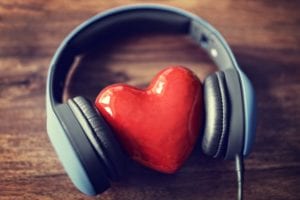 Headphones laying on a wooden table with a heart nestled in between