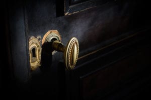 Side view detail of vintage antique brass door knob with metallic carvings and keyhole on black wooden door.
