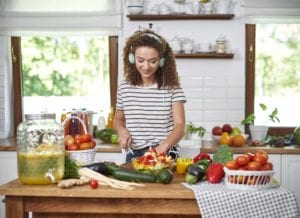 Young woman in kitchen cutting produce to cook while listening to headphones