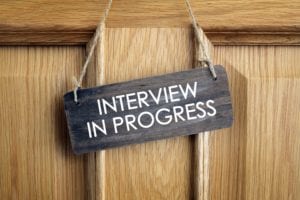Light wooden door with a small slate sign stating interview in progress hung on it.