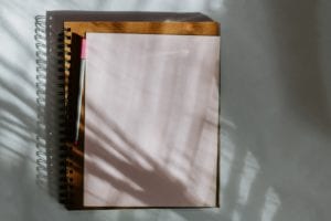 Notebook with pen and paper on a white surface with shadow cast from plants